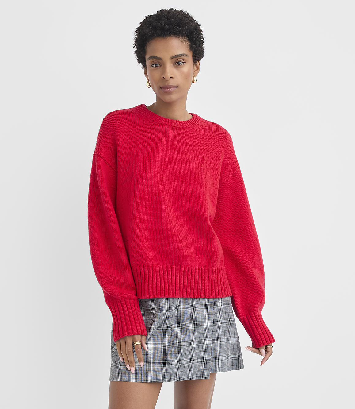 A woman in a red sweater and plaid skirt stands against a plain white background.