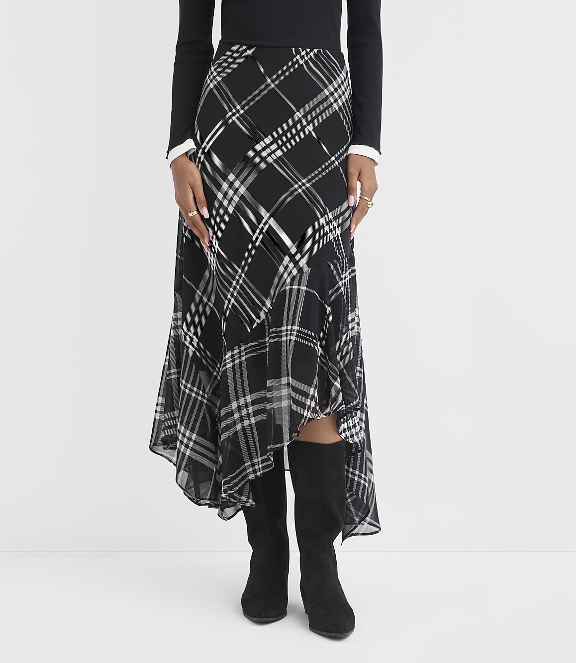 A person stands in a black and white plaid skirt with a ruffled hem and black boots, against a plain white background.