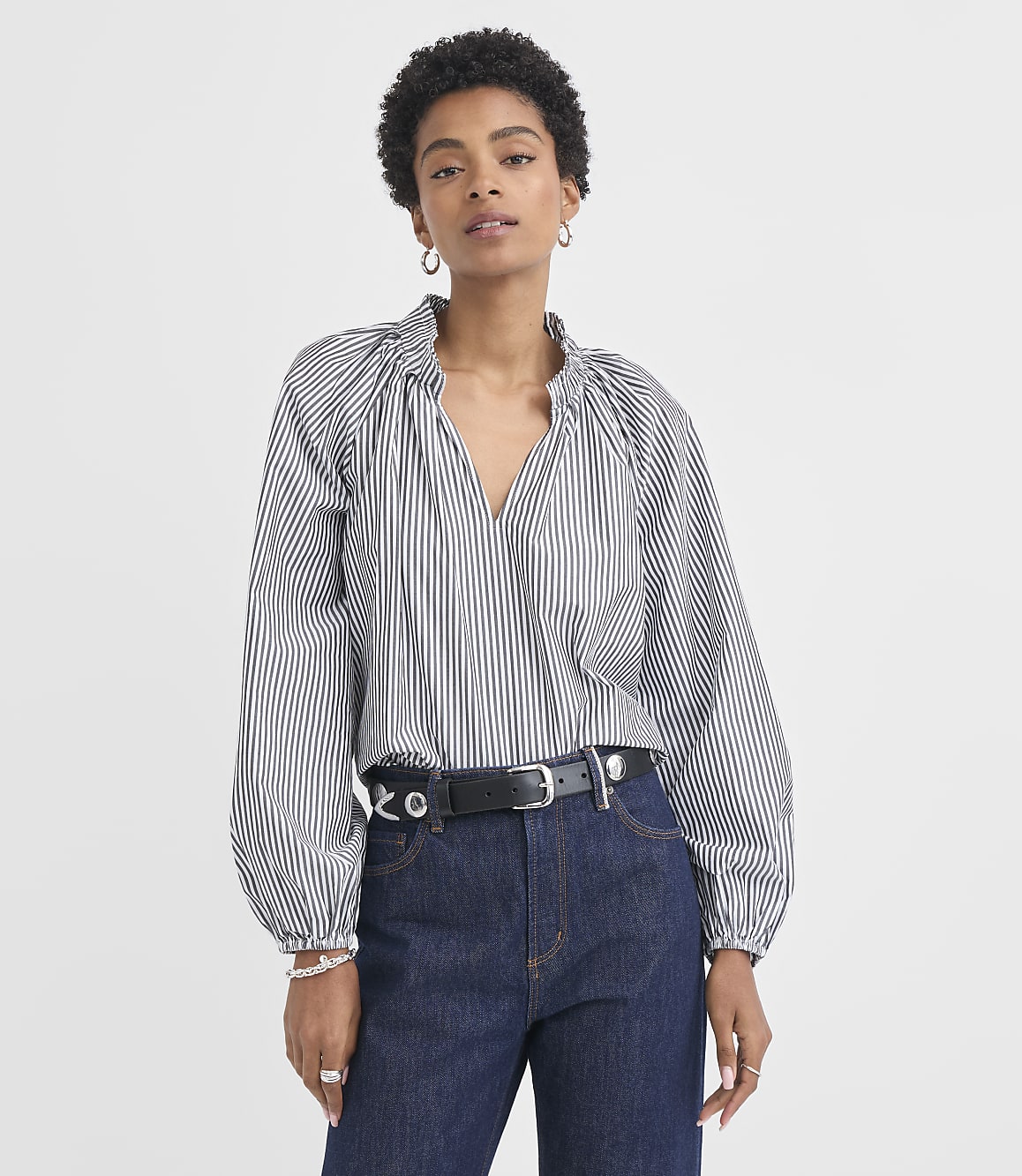 A woman in a striped blouse and jeans stands against a plain white background.
