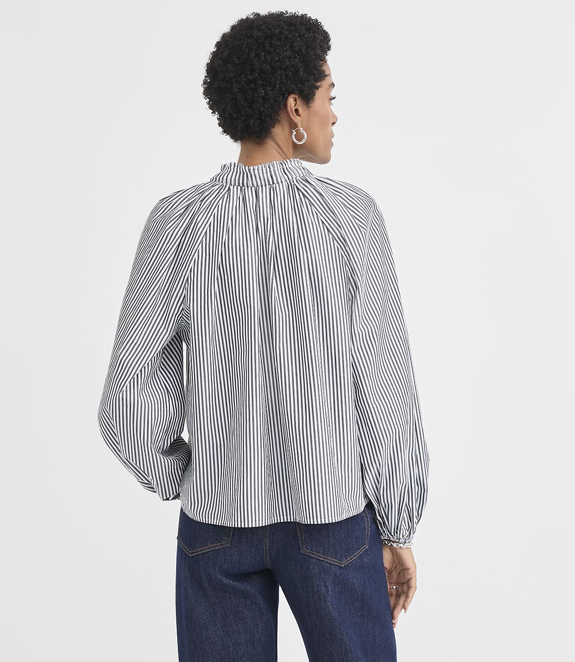 A woman wearing a black and white striped blouse and dark jeans stands against a plain white background.