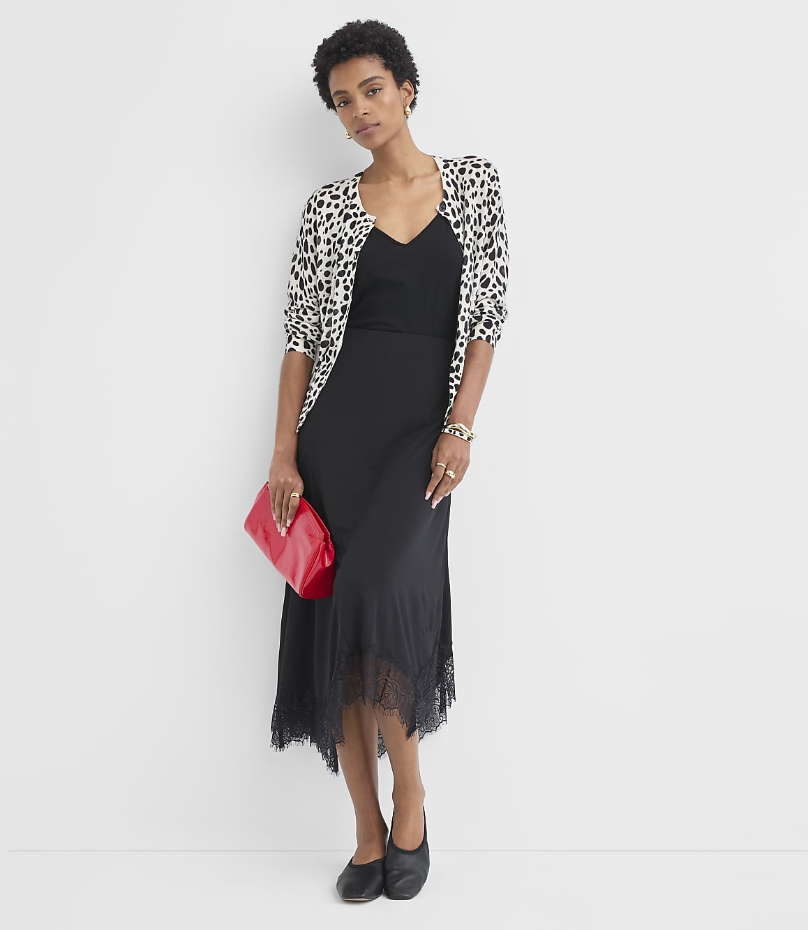 A woman in a black dress and leopard print cardigan holds a red clutch in front of a plain white background.