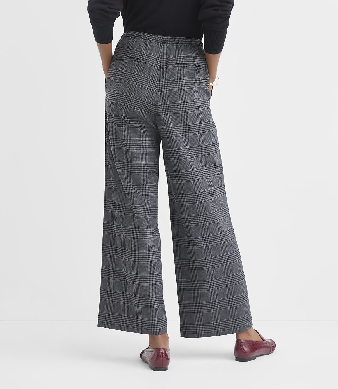 A person wearing plaid wide-leg pants and red loafers stands against a plain white background.