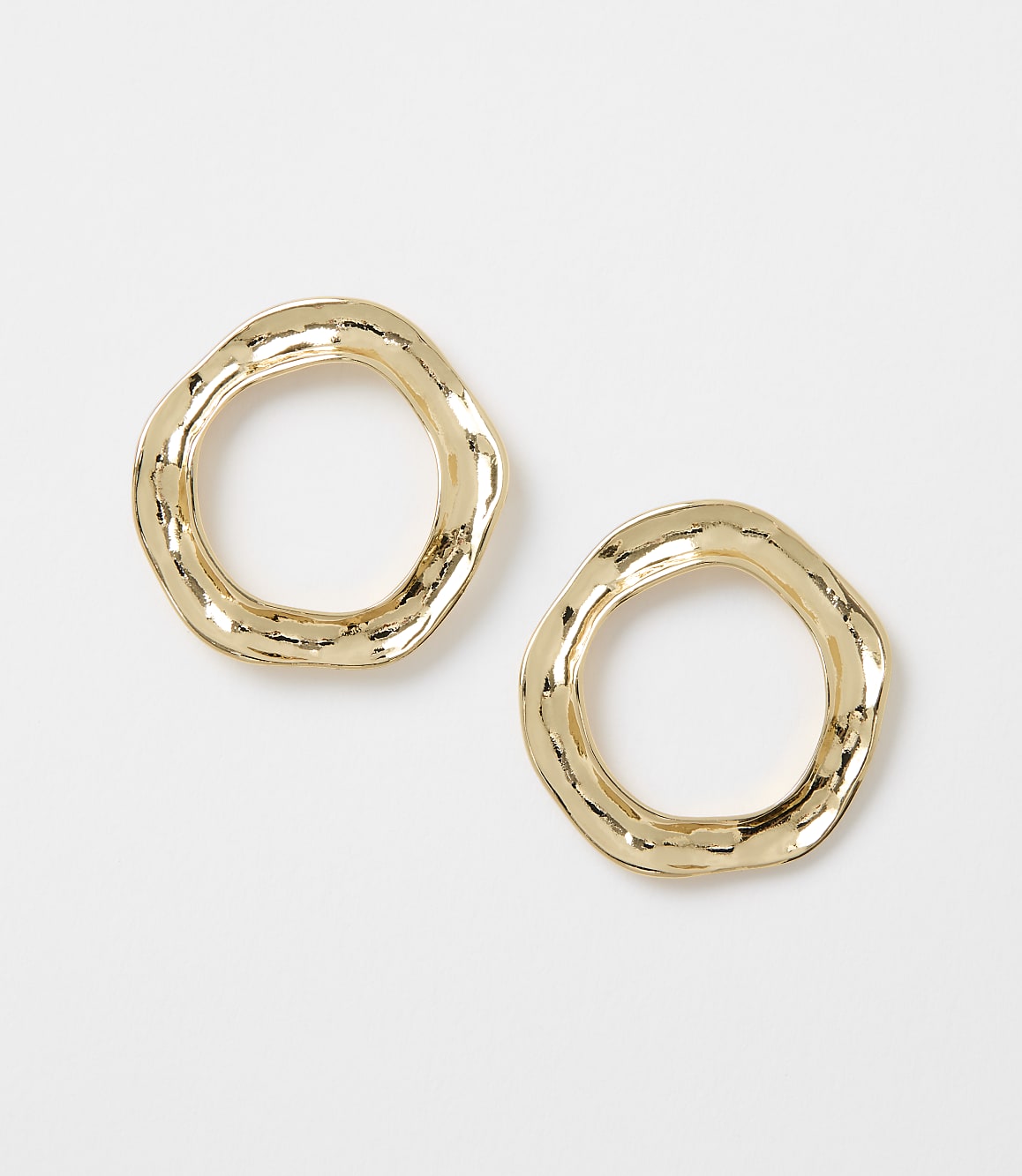 Two irregular, hammered gold hoop earrings rest on a plain white background.