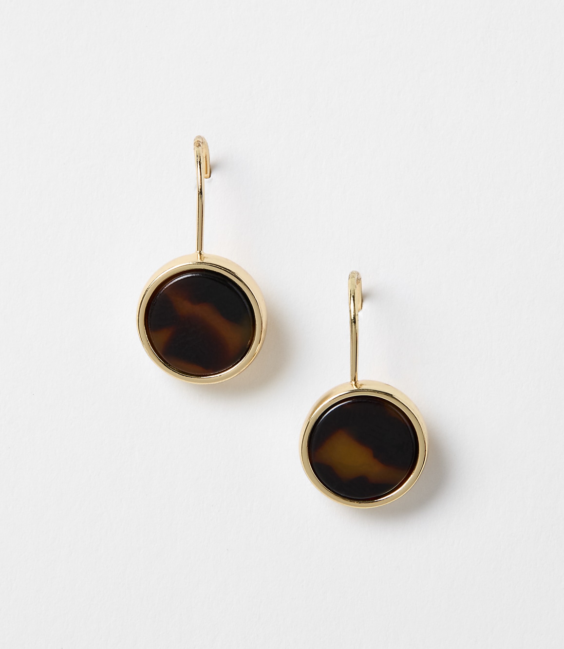 A pair of gold-rimmed tortoise shell earrings hang against a plain white background.