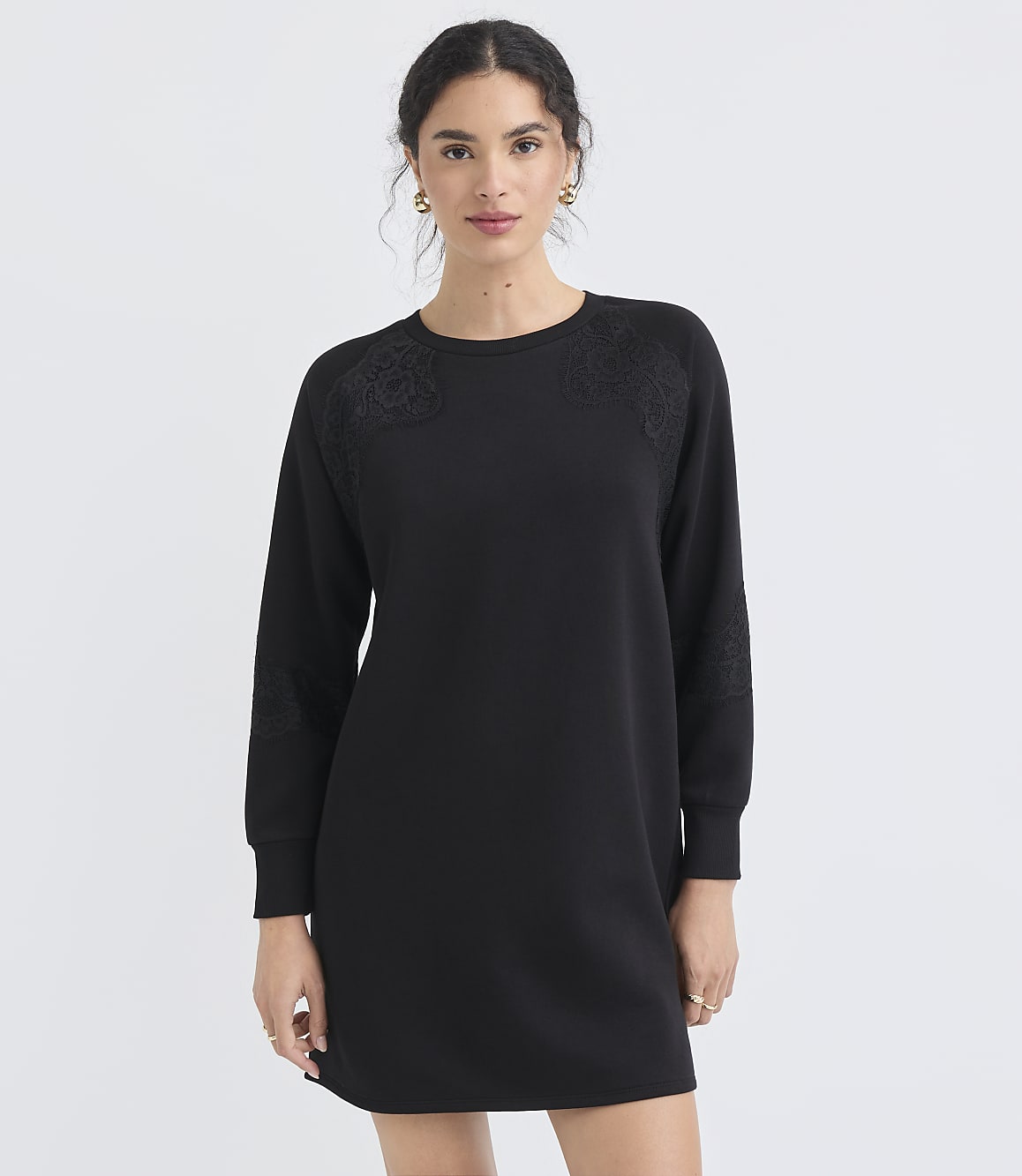 A woman in a black dress stands against a plain white background.