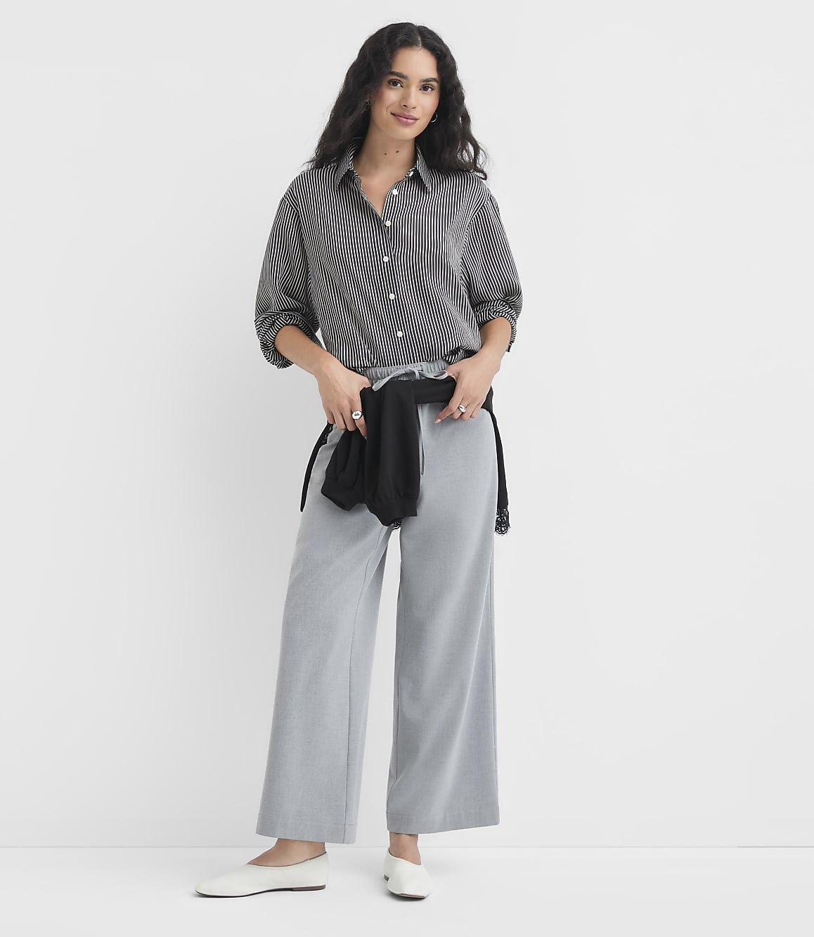 A woman in a striped shirt and wide-leg pants stands against a plain white background.
