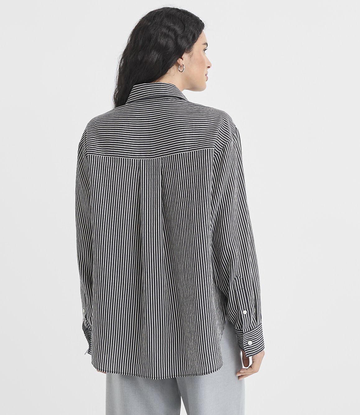 A woman in a striped shirt stands against a plain gray background.