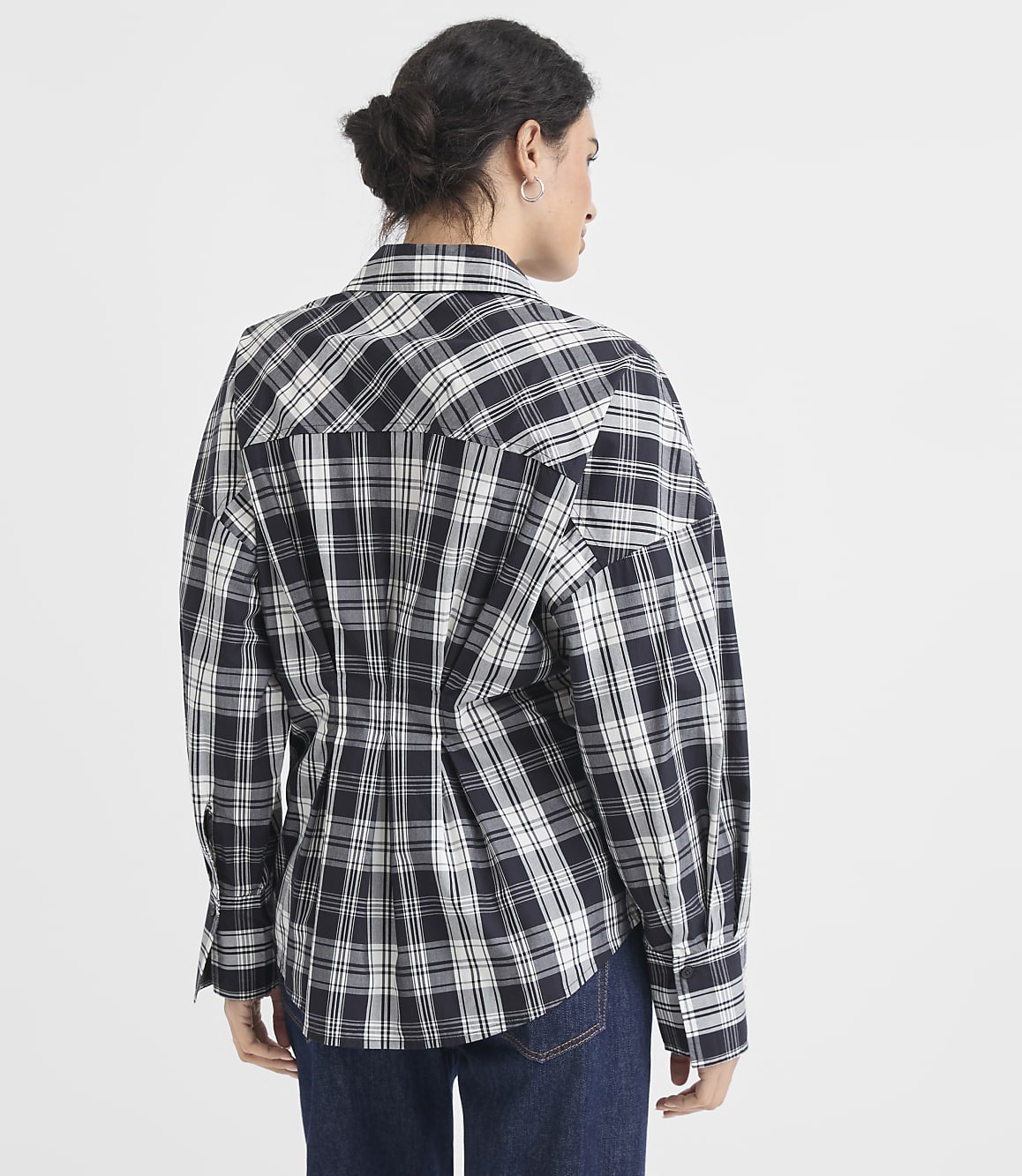 A woman in a black and white plaid shirt stands against a plain white background.
