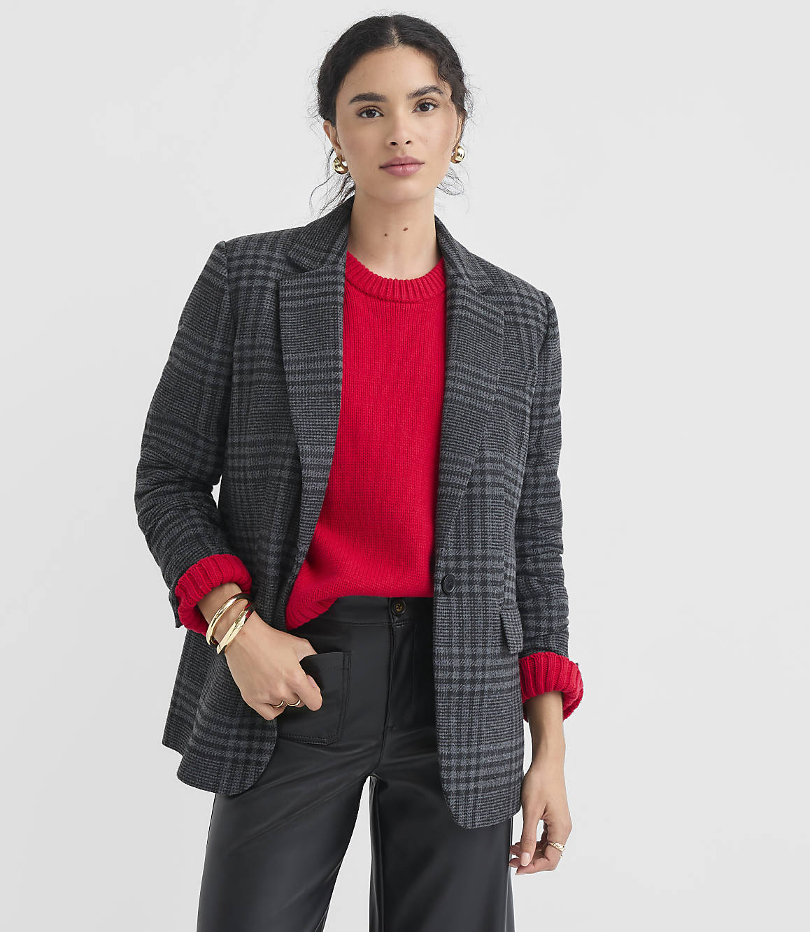 A woman in a red sweater and plaid blazer stands against a plain white background.