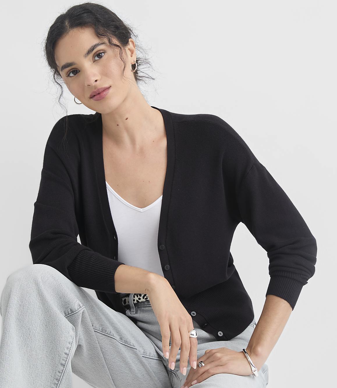 A woman in a black cardigan and white top poses against a plain white background.