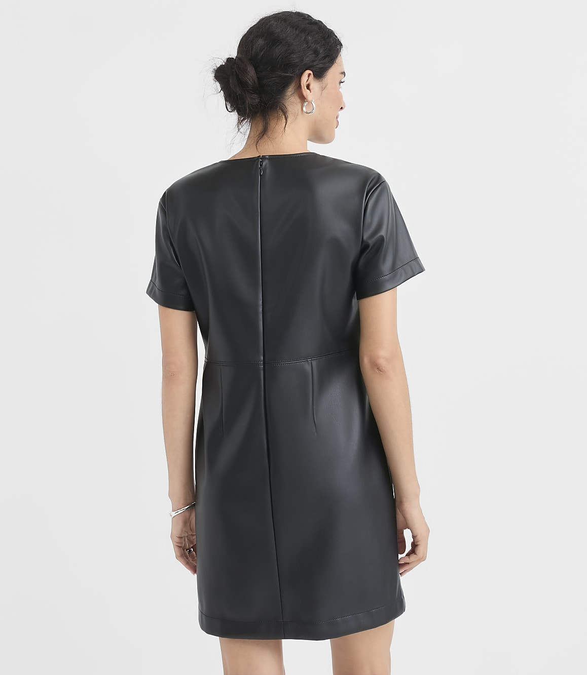A woman in a black faux leather dress stands against a plain white background.