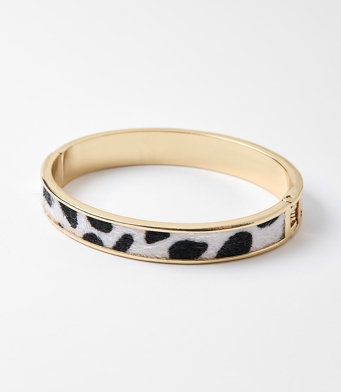 A gold bangle bracelet with a cow print fuzzy inlay rests on a plain white background.