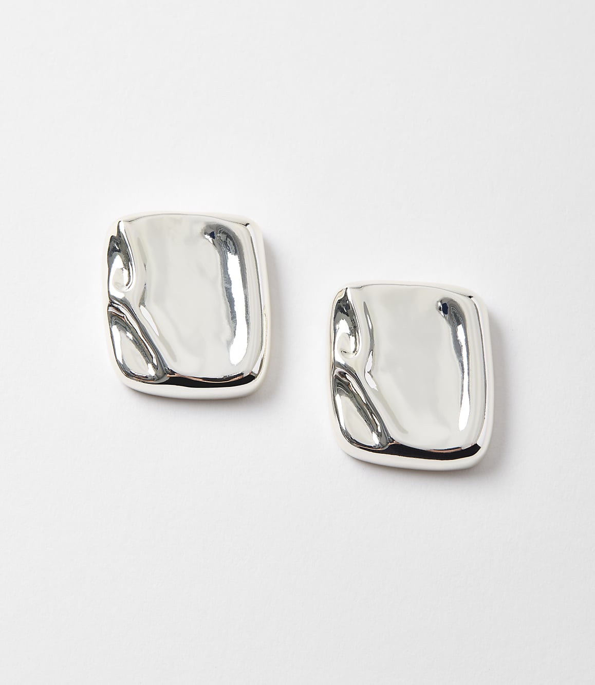 Two abstract, silver square earrings with a molten appearance rest on a plain white background.