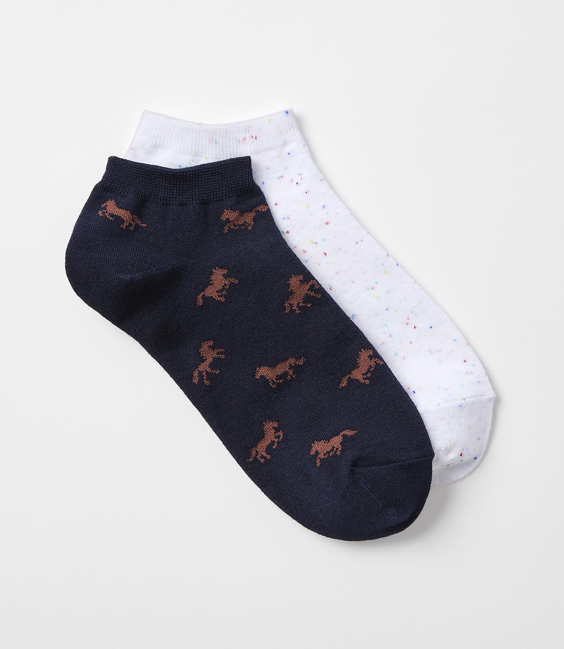 A pair of ankle socks, one navy with a horse pattern and the other white with colorful speckles, rests on a plain white background.