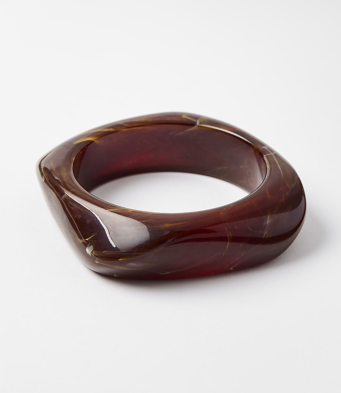 A chunky, translucent amber-colored bangle with swirling patterns rests on a plain white background.