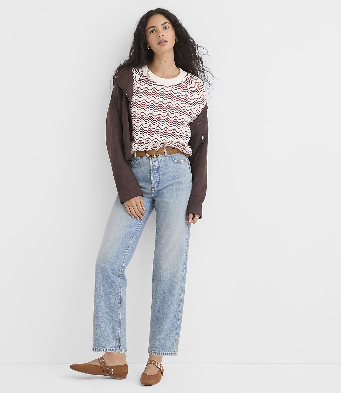 A woman in a patterned sweater and jeans stands against a plain white background.