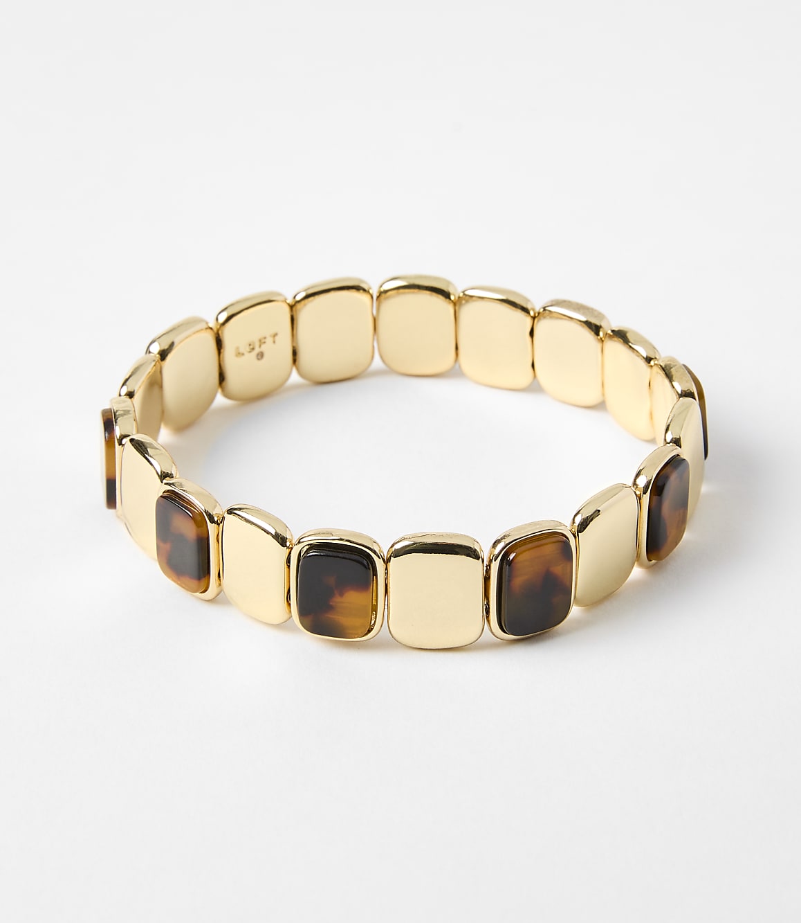 A gold bracelet with square tortoise shell accents rests on a plain white background.
