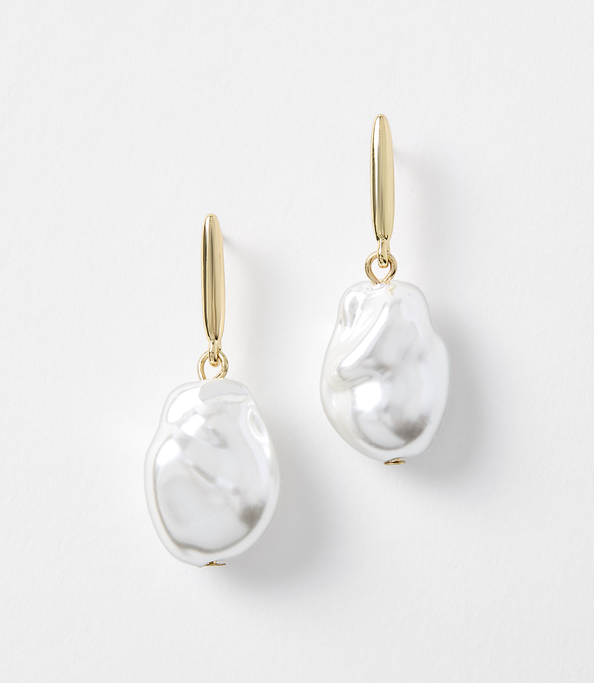 A pair of gold hoop earrings with irregular white pearls hang against a plain white background.