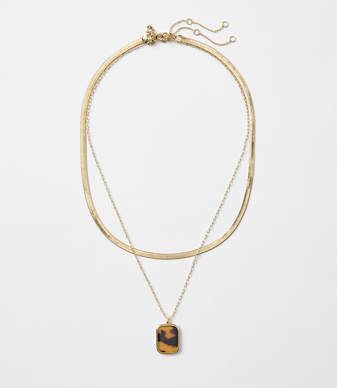 A layered gold necklace with a tortoise shell pendant hangs against a plain white background.