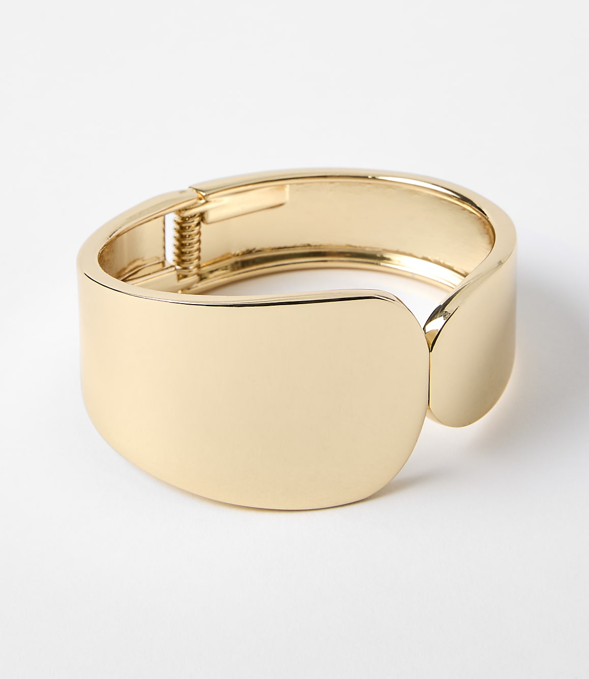 A polished gold cuff bracelet with a hinge closure rests on a plain white background.