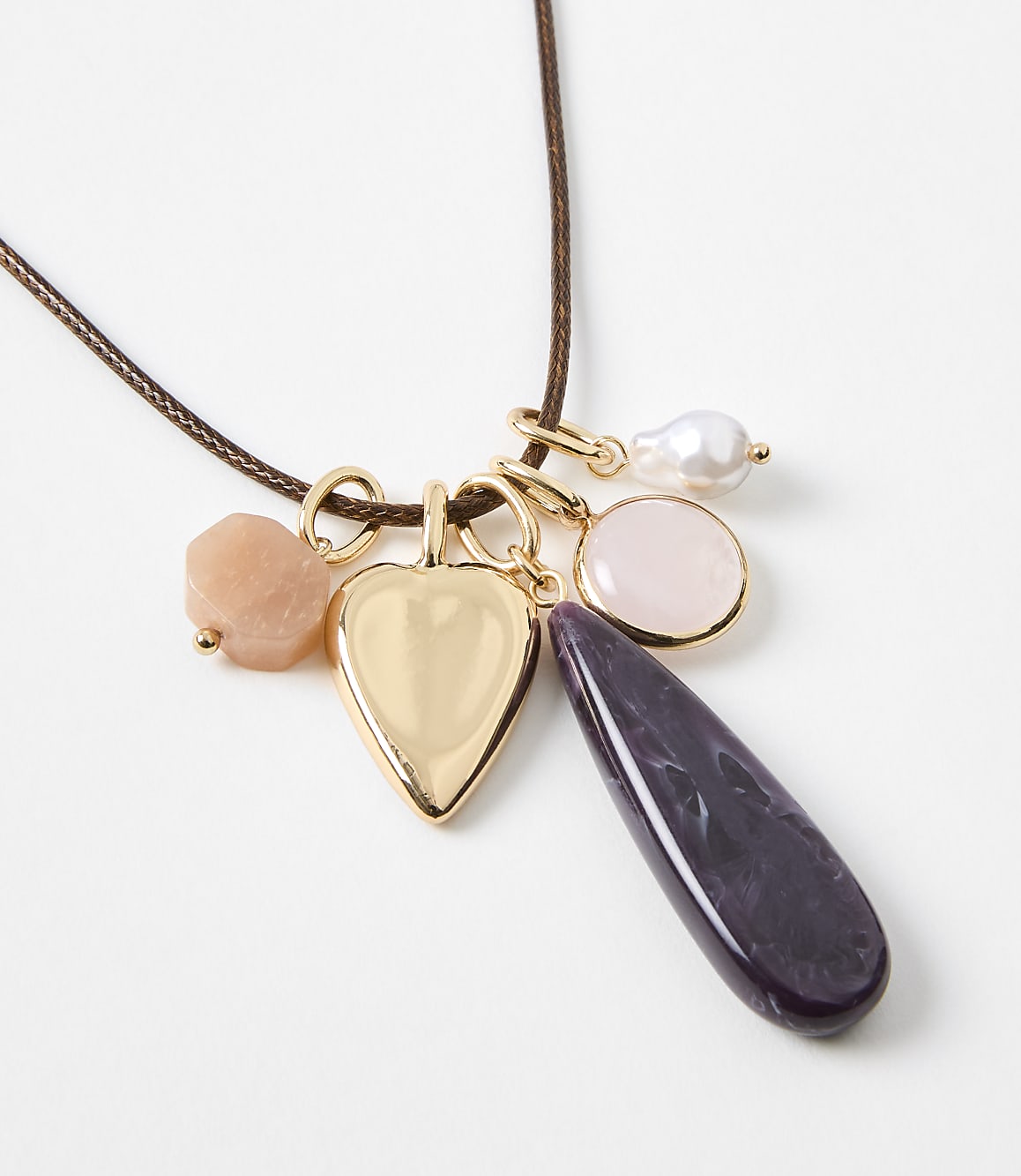 A gold heart locket and various colorful gemstone charms hang from a brown cord against a plain white background.