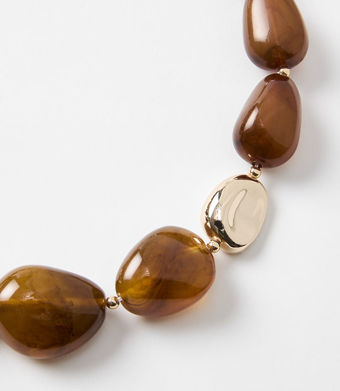 A close-up of a chunky, amber-colored beaded necklace with gold accents rests against a plain white background.