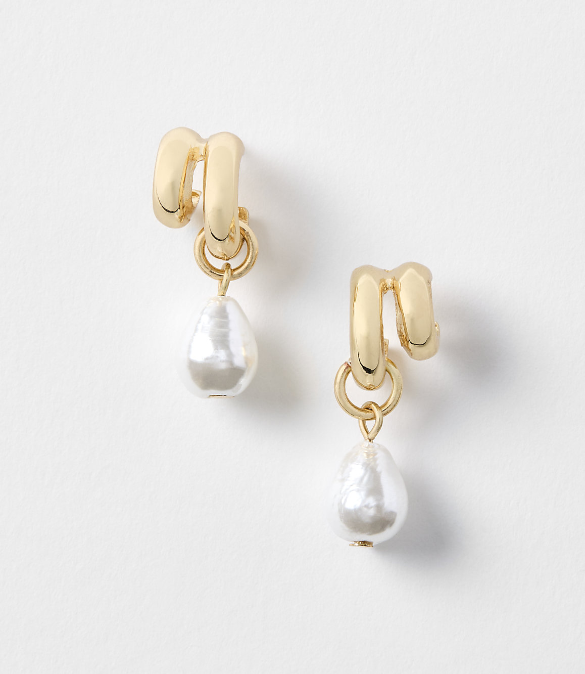 A pair of gold earrings with pearl drops hang against a plain white background.