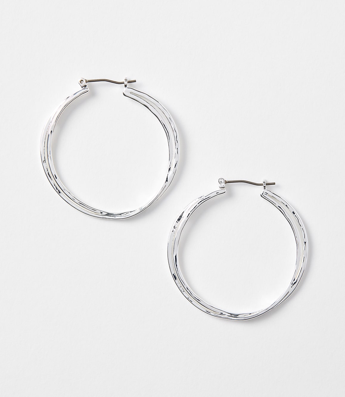Two silver hoop earrings with textured surfaces rest on a plain white background.