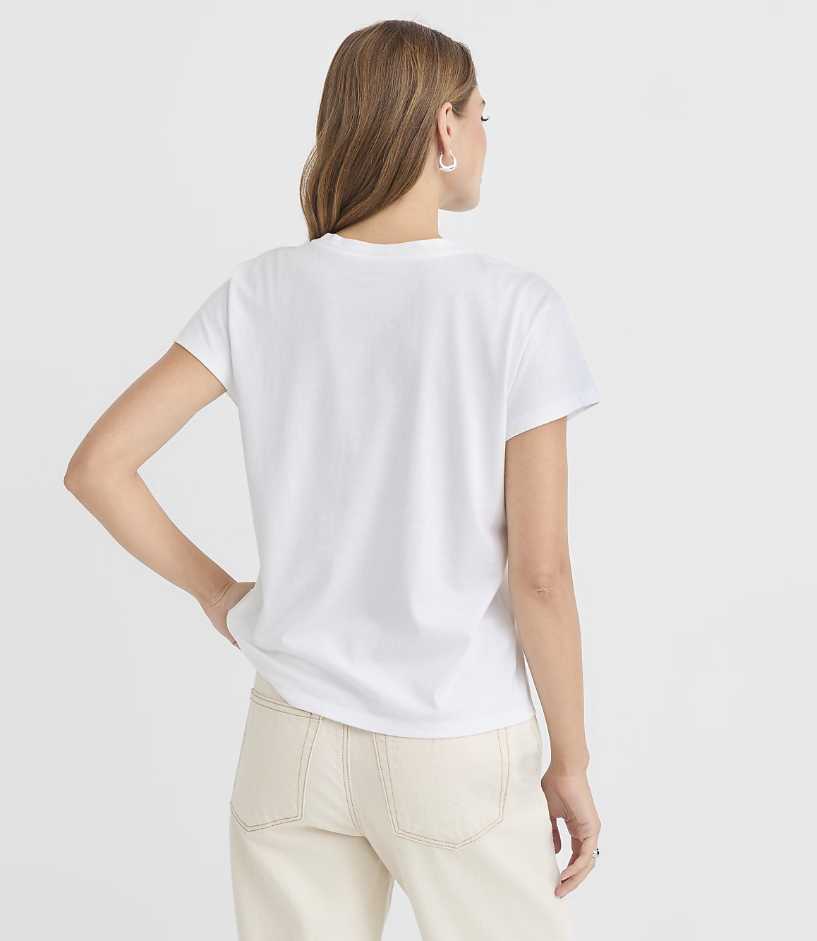 A woman in a white t-shirt and light-colored pants stands against a plain white background.