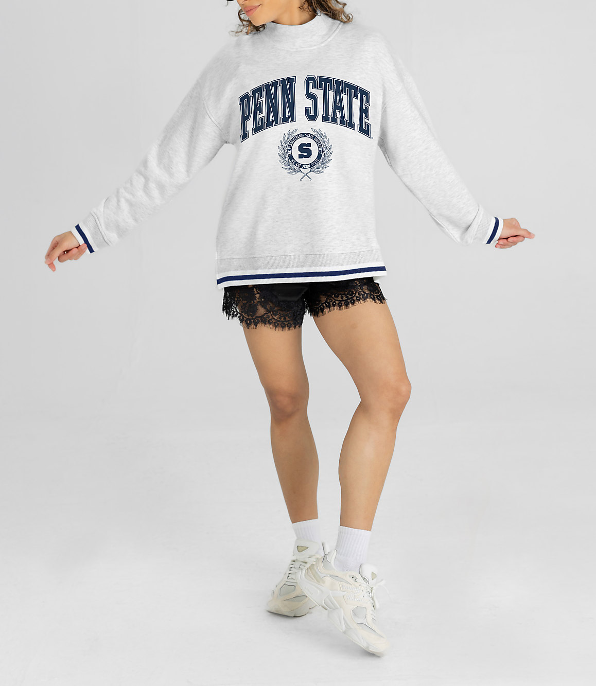 A woman in a Penn State sweatshirt and lace shorts stands against a plain white background.