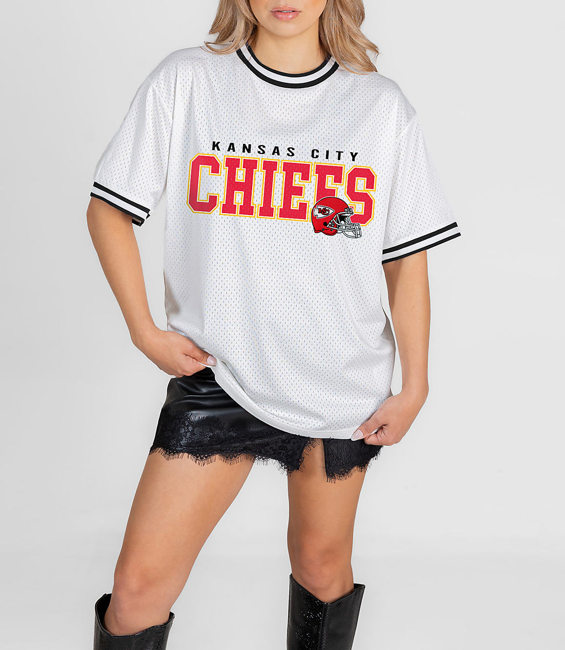 A woman in a white Kansas City Chiefs jersey and black skirt stands against a plain white background.