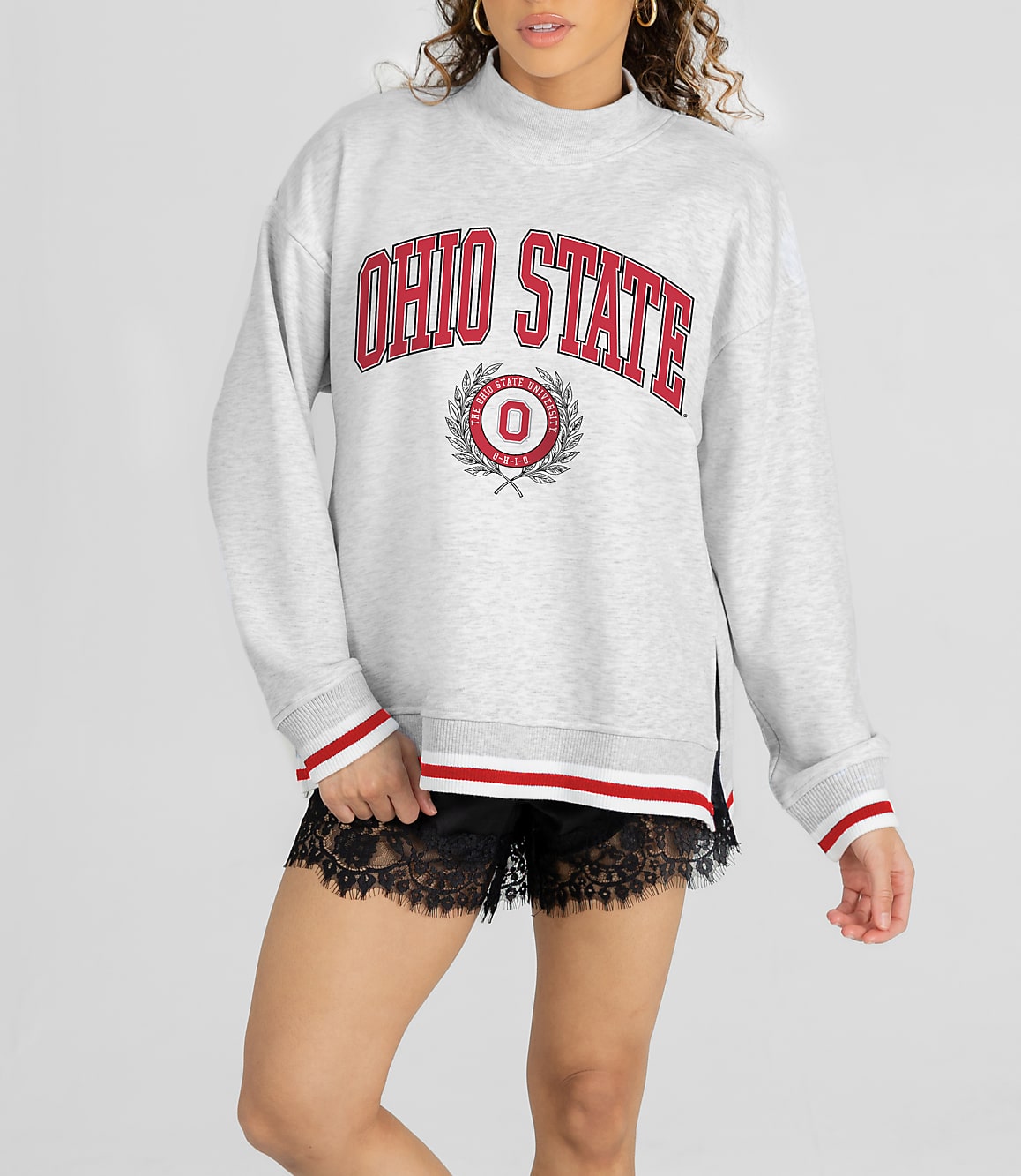 A woman in a grey Ohio State sweatshirt and black lace shorts stands against a white background.