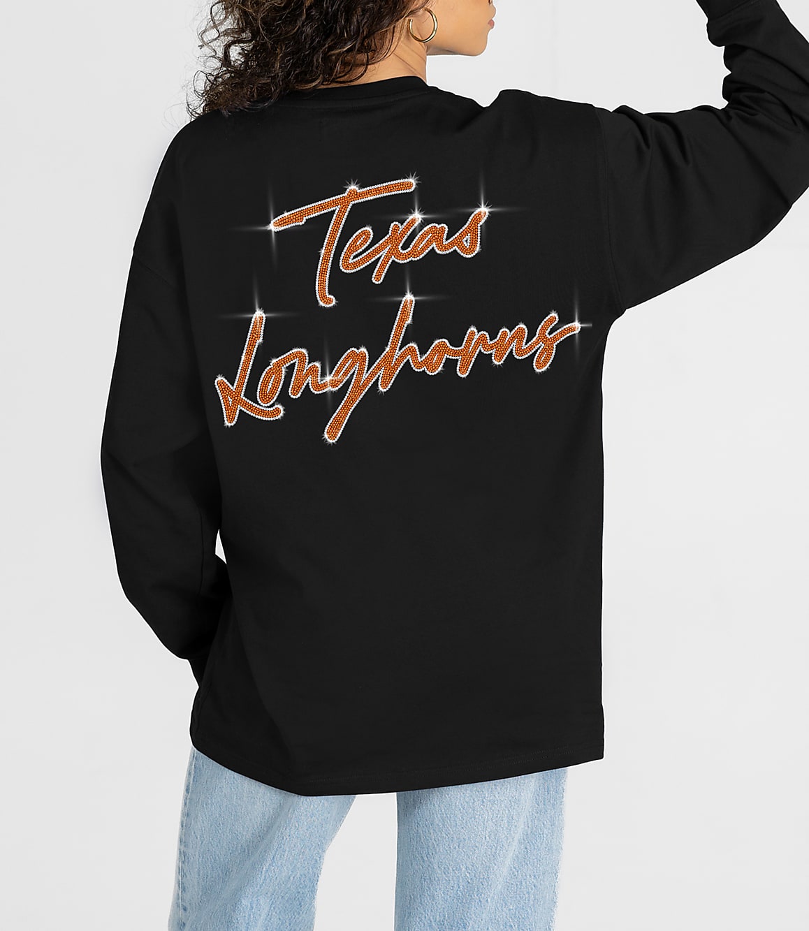 A person in a black long-sleeved shirt with "Texas Longhorns" written in glittery orange script on the back stands against a plain white background.