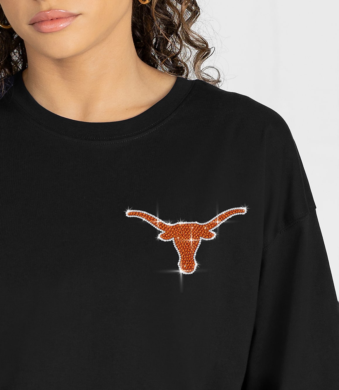 A close-up of a person wearing a black t-shirt with a sparkling Texas Longhorns logo on the chest, with a blurred background.