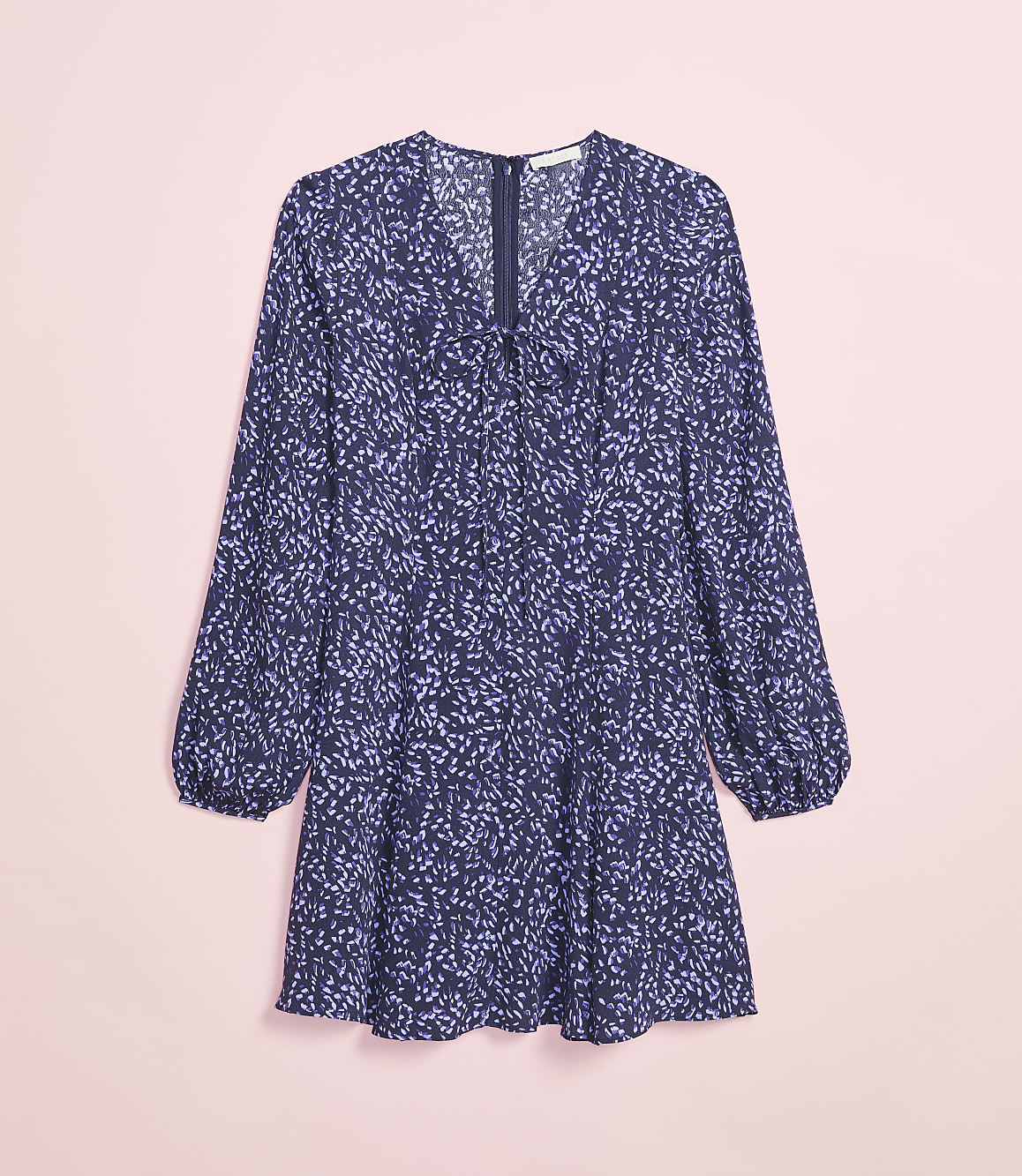 A long-sleeved navy blue dress with a scattered light purple floral print lies flat against a soft pink background.