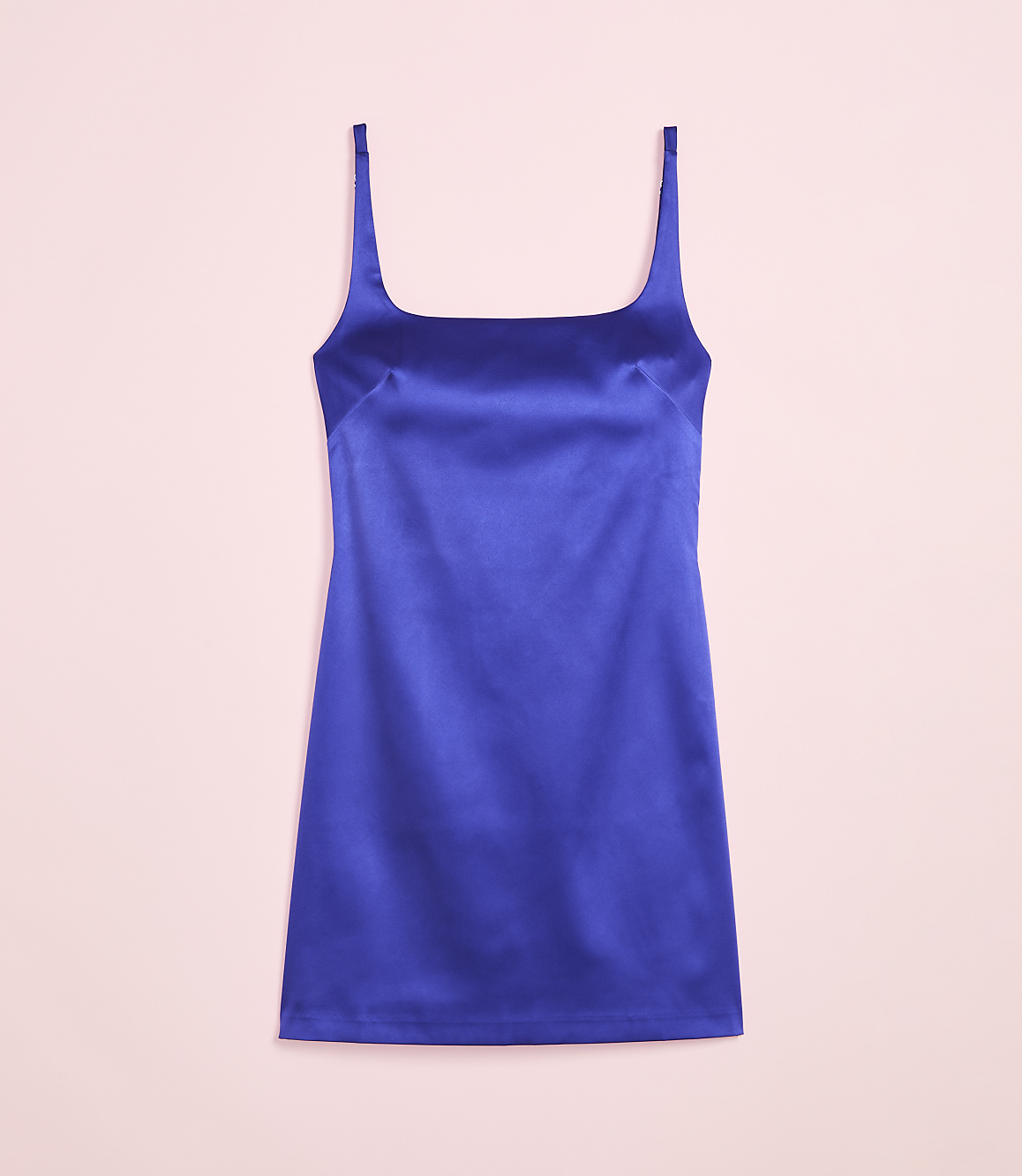 A vibrant blue satin slip dress with thin straps is laid flat against a soft pink background.