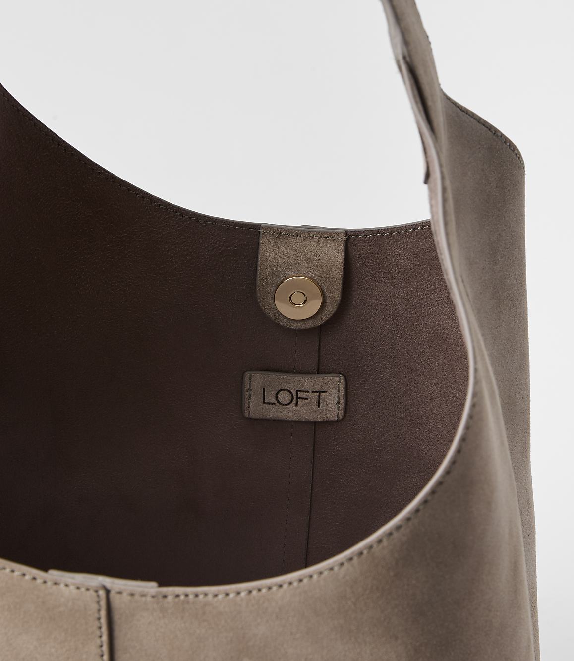 A taupe suede hobo bag with a gold snap closure and a LOFT logo tag is shown against a plain white background.