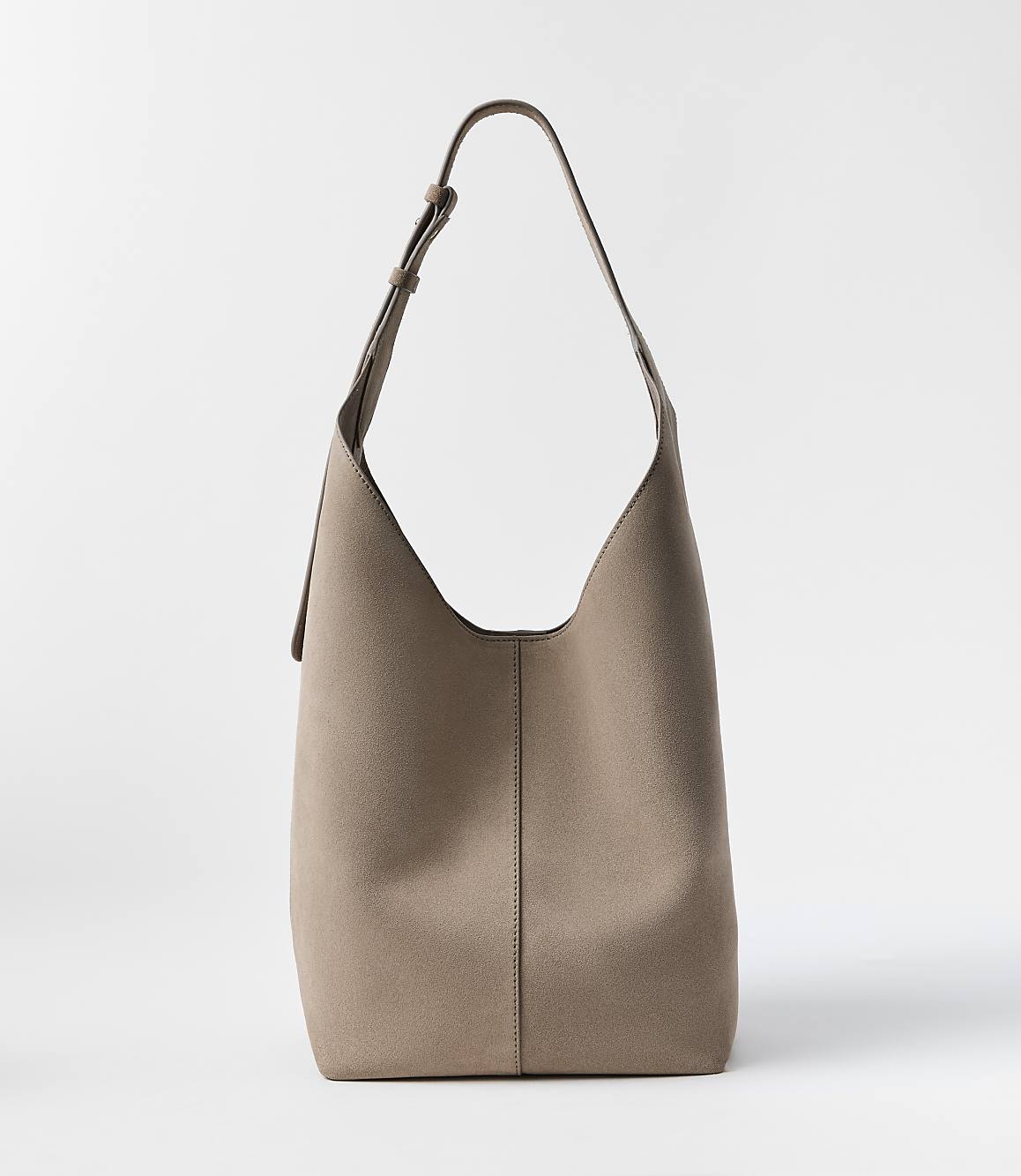 A taupe leather hobo bag with a single strap stands against a plain white background.