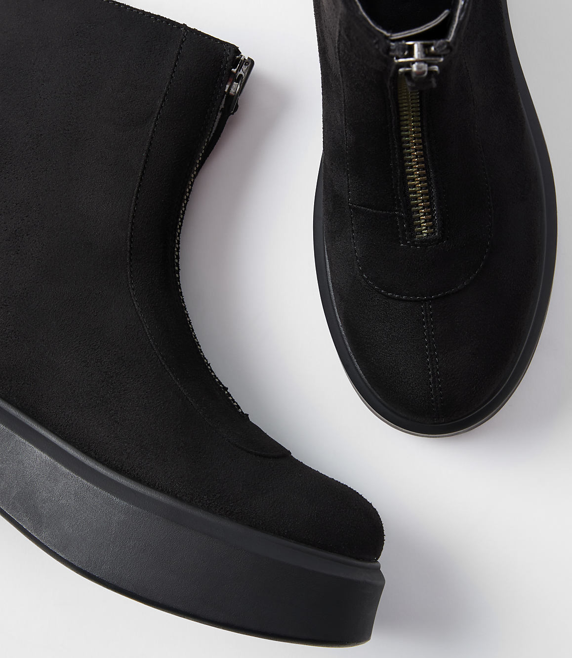 A pair of black suede ankle boots with front zippers rests on a white surface.