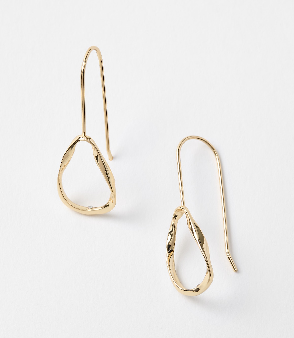 A pair of gold abstract hoop earrings hang against a plain white background.