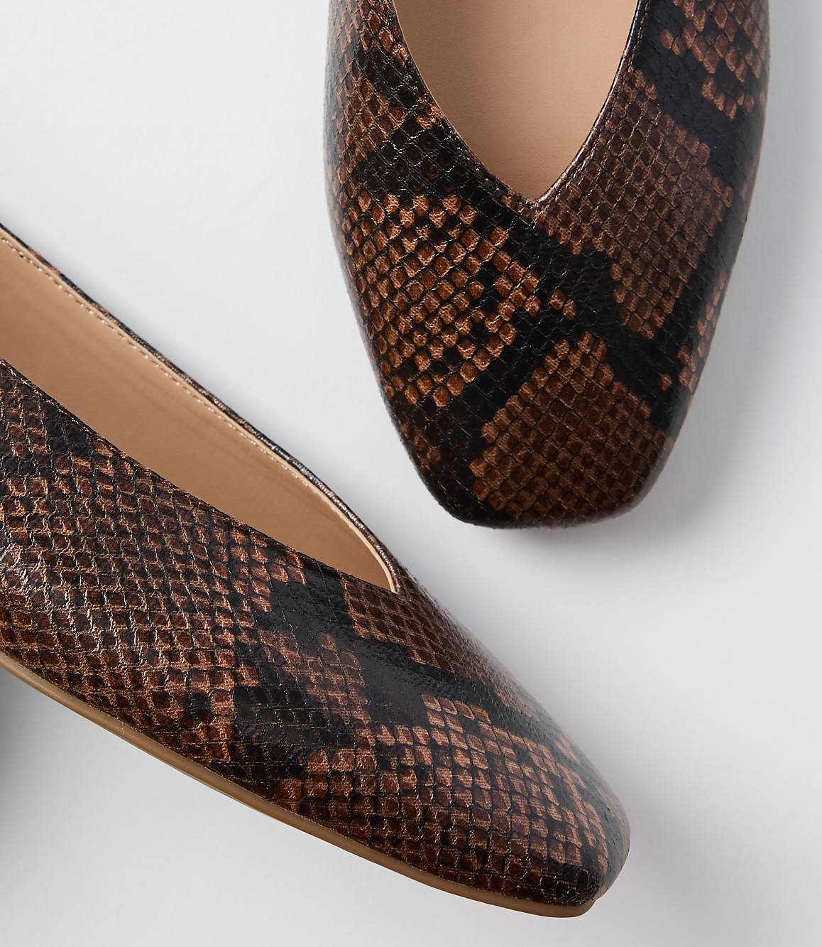 A pair of brown snakeskin pointed-toe flats rests on a plain white background.