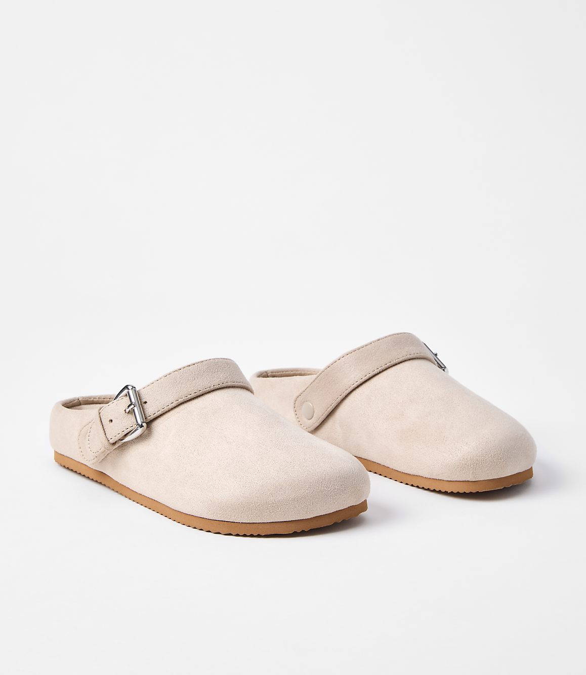 A pair of light pink clogs with tan straps and buckles rests on a white background.