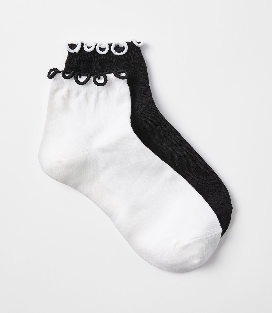 A pair of white and black ankle socks with ruffled cuffs are laid out on a plain white background.
