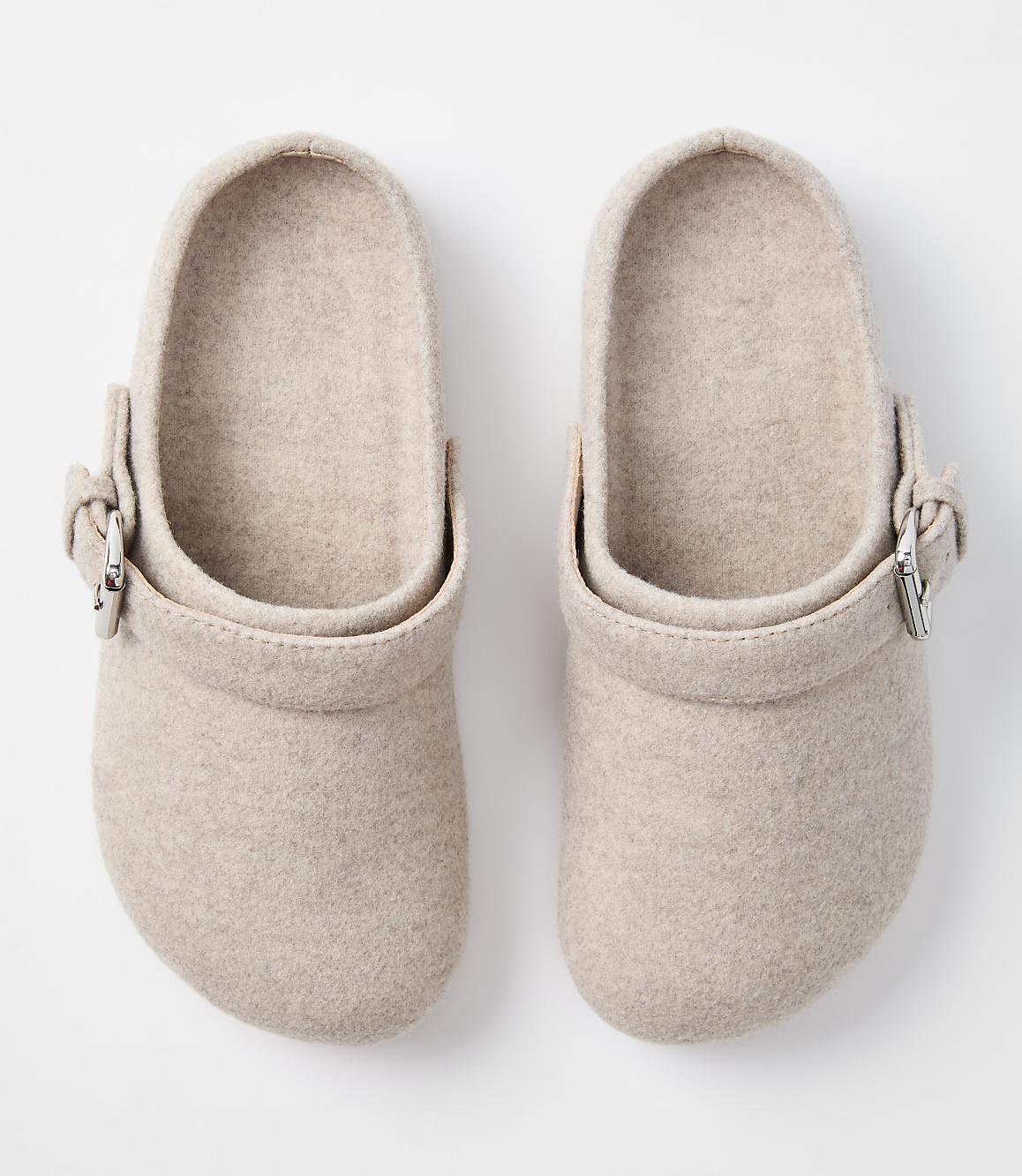 A pair of beige felt clogs with silver buckles are displayed against a plain white background.