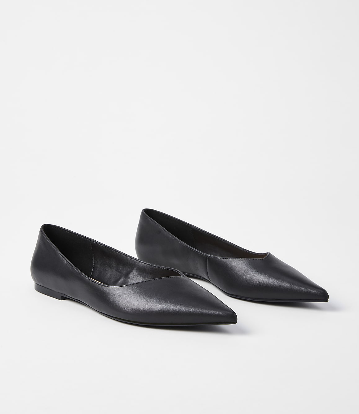 A pair of black pointed-toe flats rests on a plain white background.
