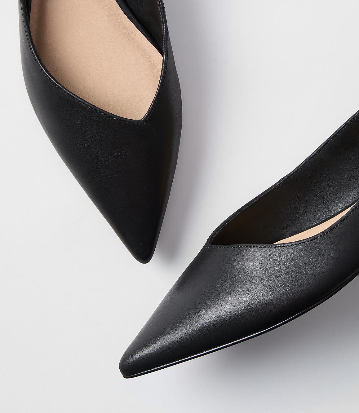 Two black pointed-toe flats with light beige insoles rest on a plain white background.