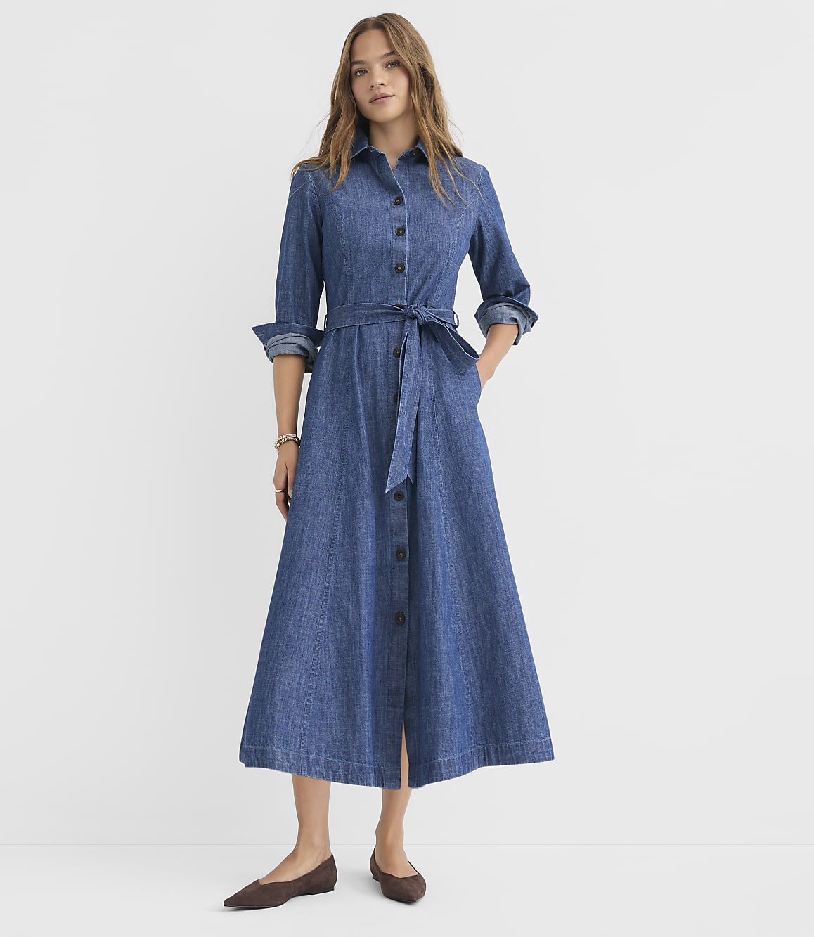 A woman in a denim shirt dress stands against a plain white background.