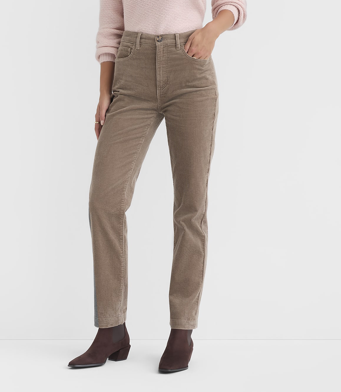 A person in a pink sweater and tan corduroy pants stands against a plain white background.
