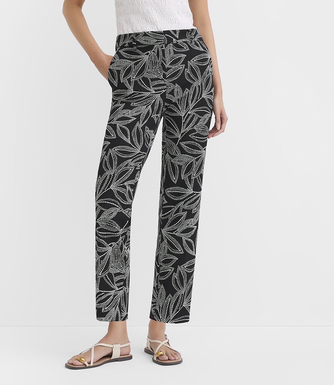A person models black pants with a white leaf pattern, standing against a plain white background.