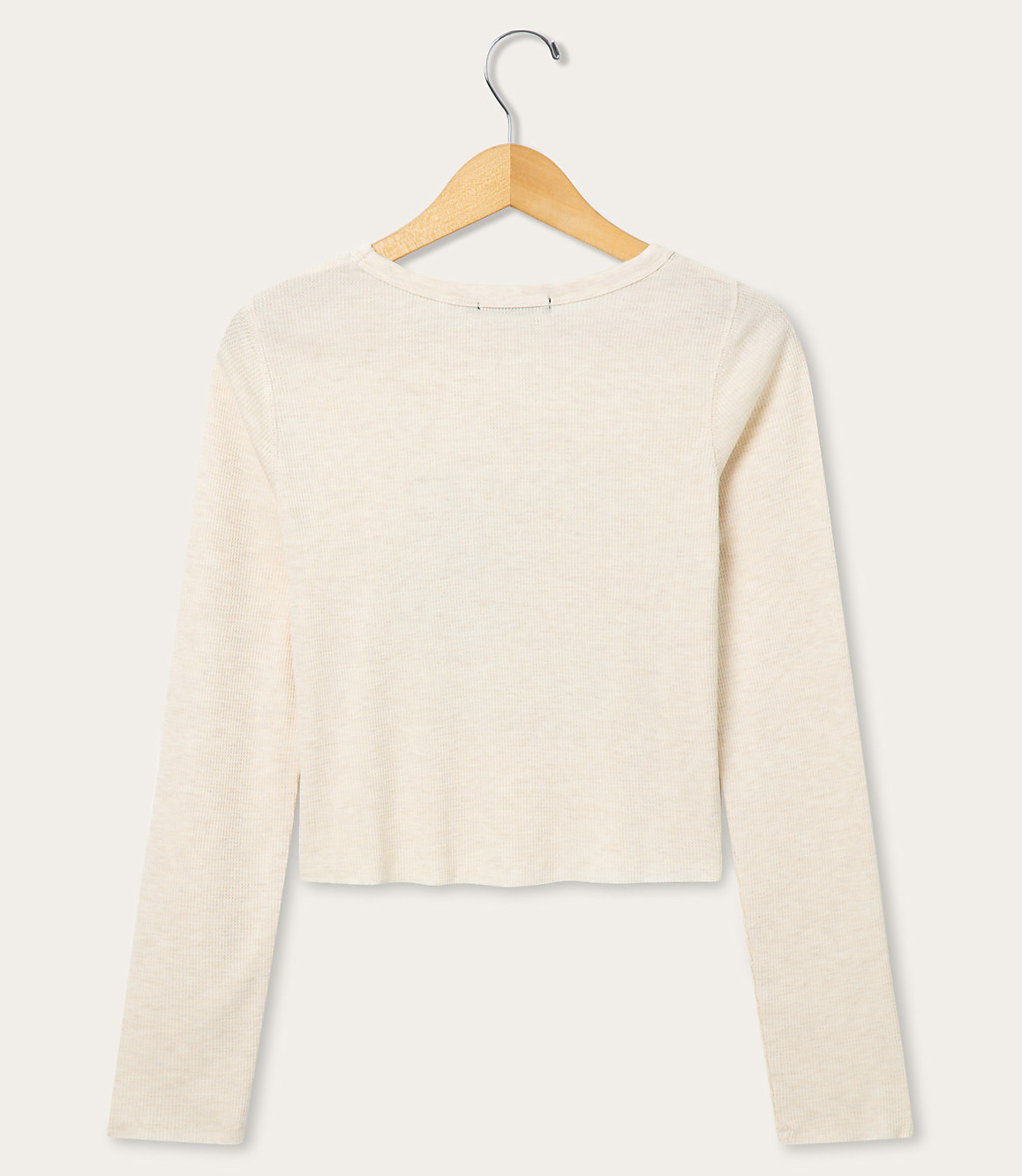 A cream-colored long-sleeved shirt hangs on a wooden hanger against a plain white background.